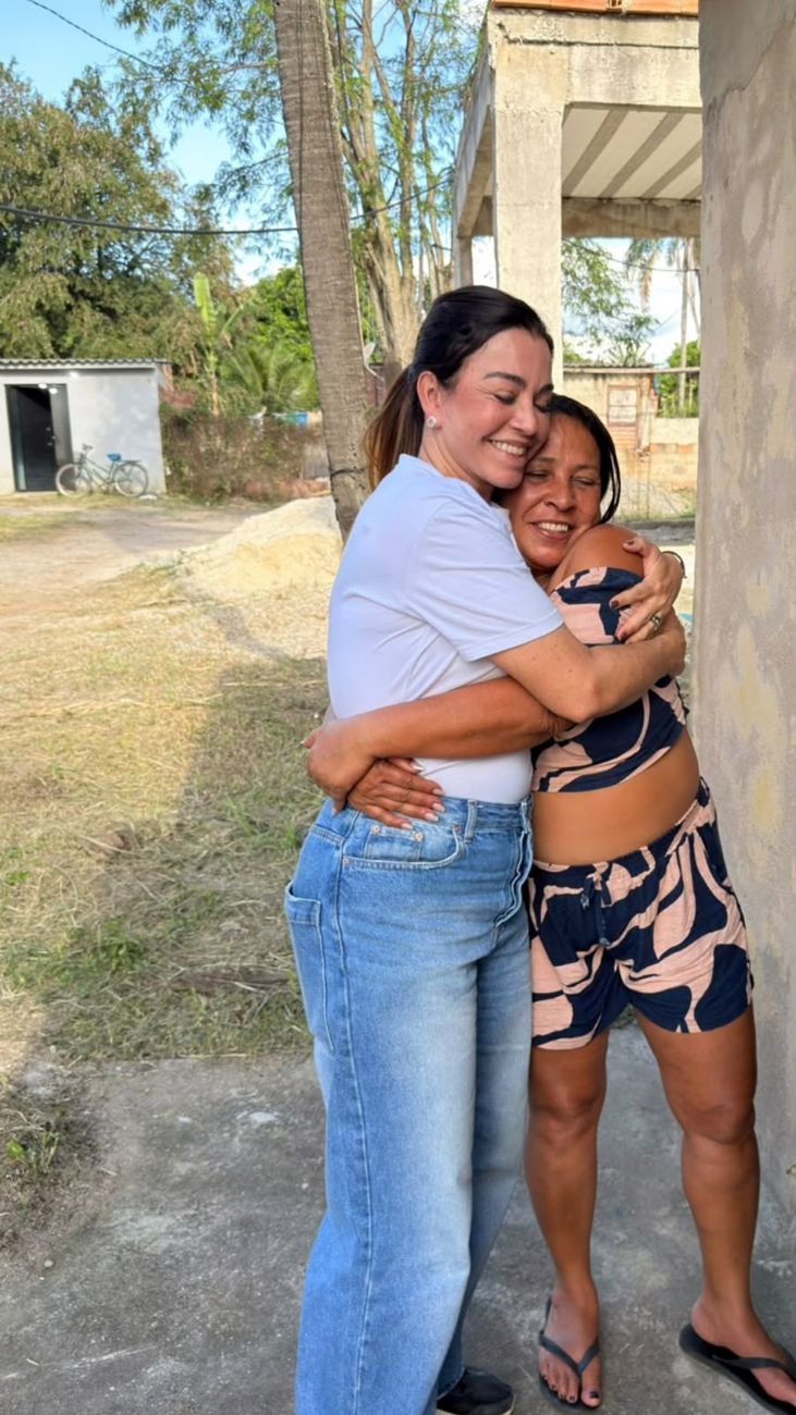 Kelaine abraçada com uma moradora, as duas sorrindo de olhos fechados