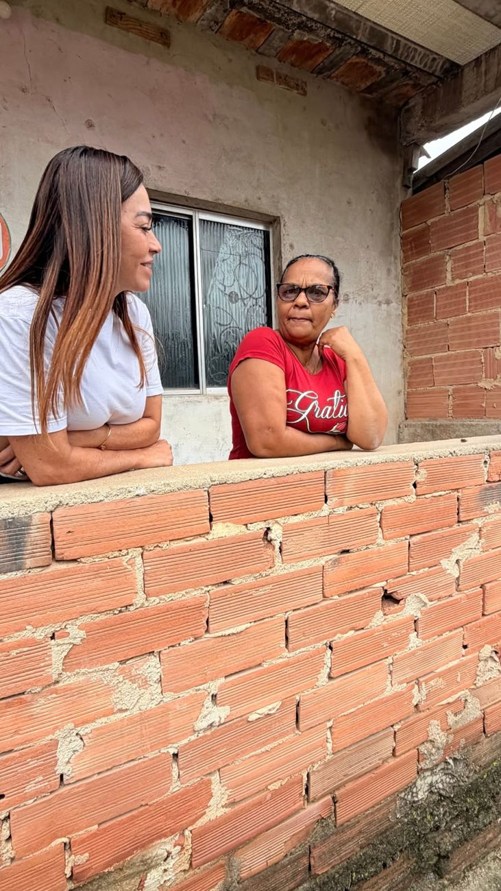 Kelaine conversa com uma moradora apoiada no muro de casa